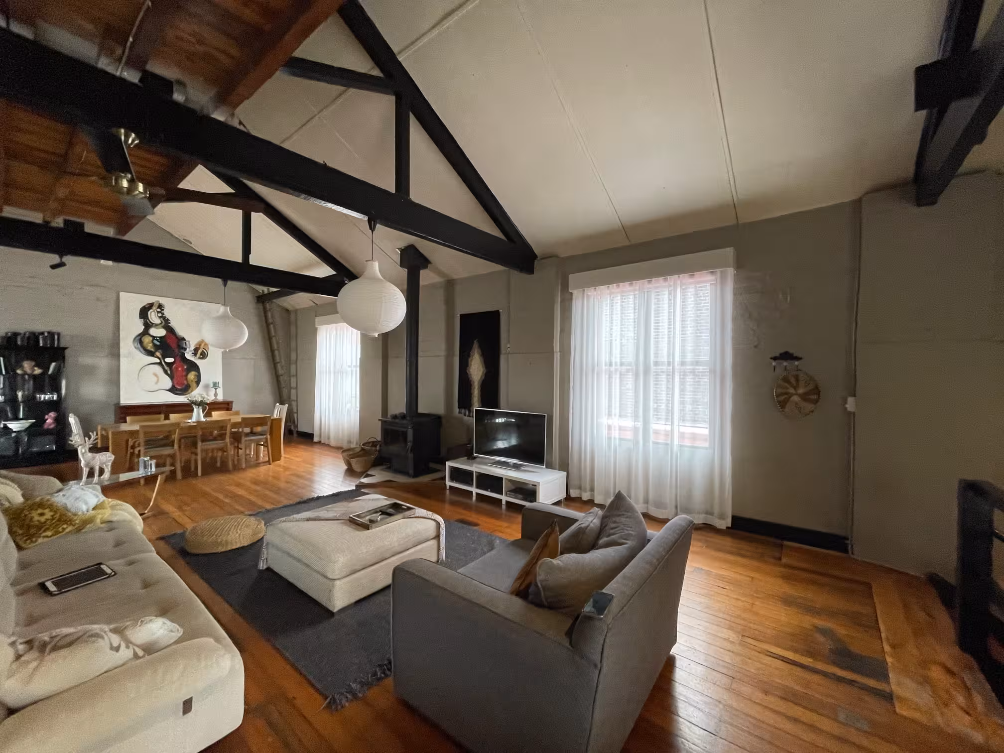 Sheer curtains framing a tall window in a living room with exposed timber beams and polished hardwood floors